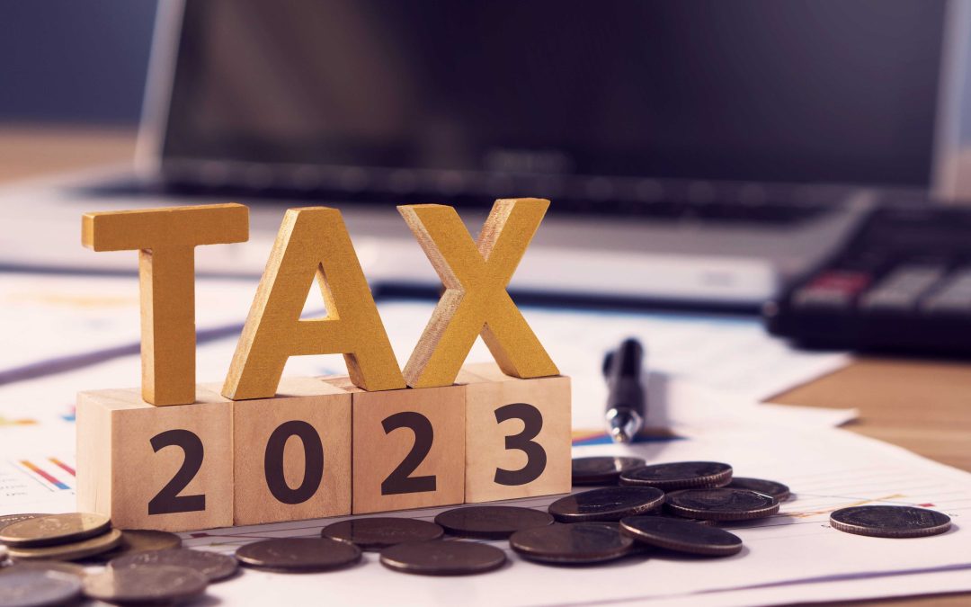 Wood blocks spelling out "tax 2023" sit on top of papers and coins on a desk.