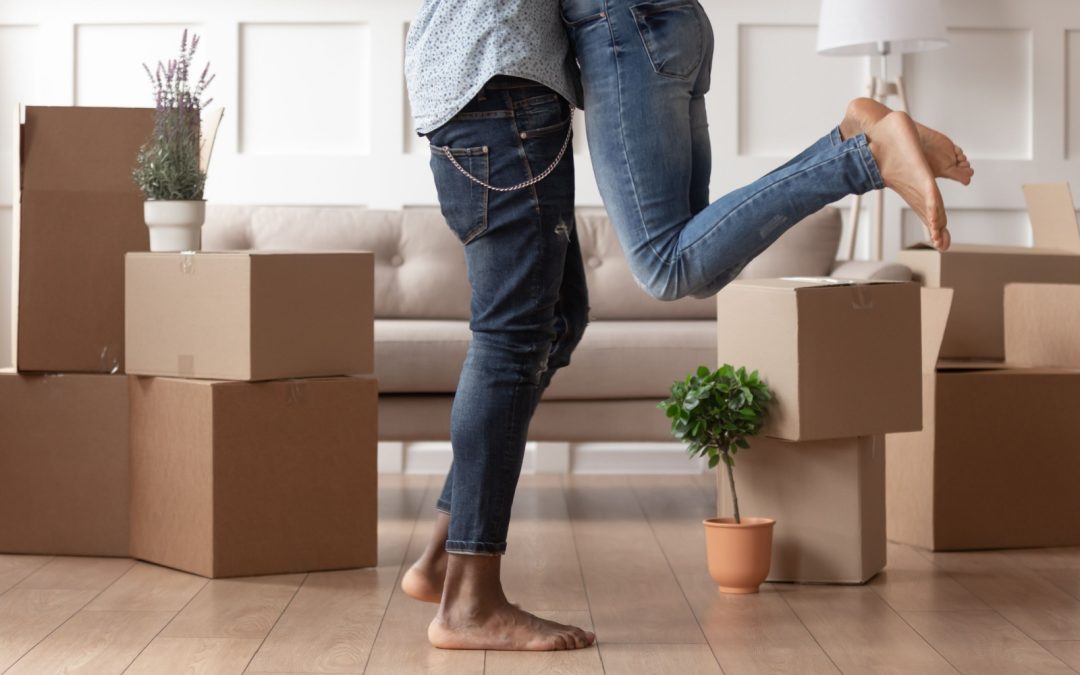The bottom half of a couple hugging with boxes beside their feet after buying their first home.