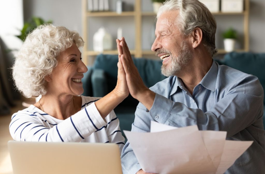 A married senior couple smiles and high-fives while looking over their retirement paperwork.