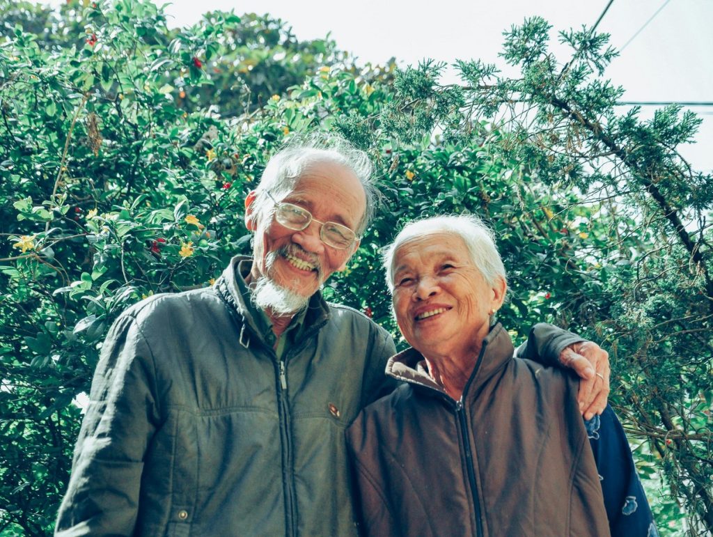elderly couple embracing in a garden smiling at the camera