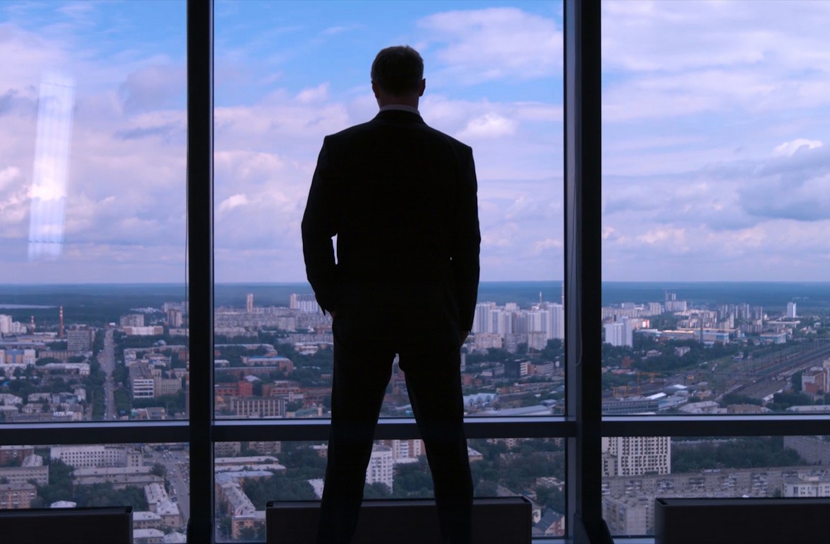 business owner looking out his office through a glass window at the city
