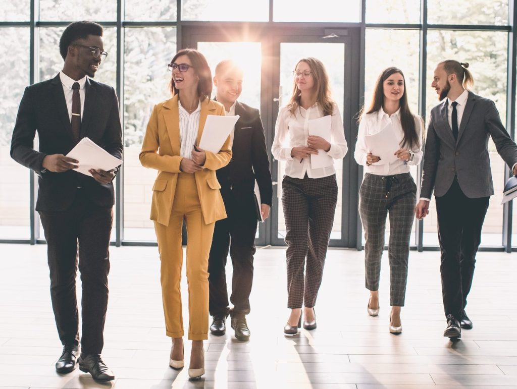 corporate work team walking through a lobby with big glass windows and doors in the background