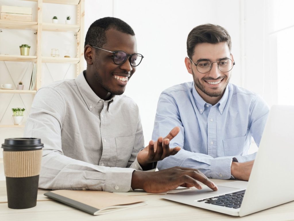 two cowrokers looking at a laptop and working together while drinking coffee